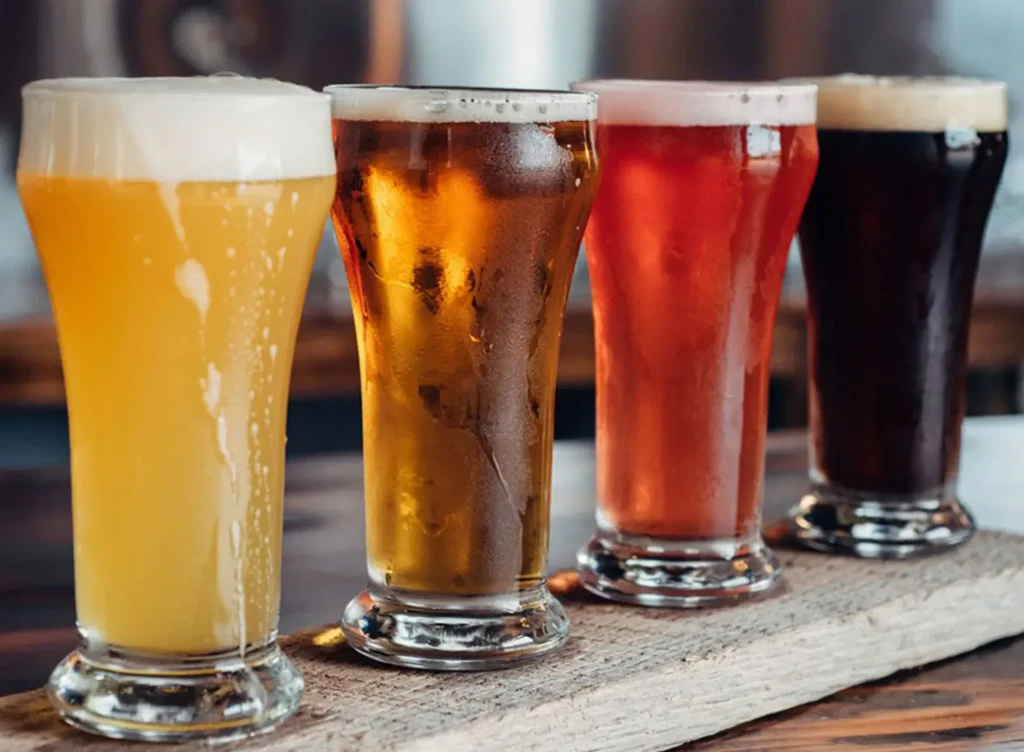 Four distinct beers in a flight on a rustic wooden surface.