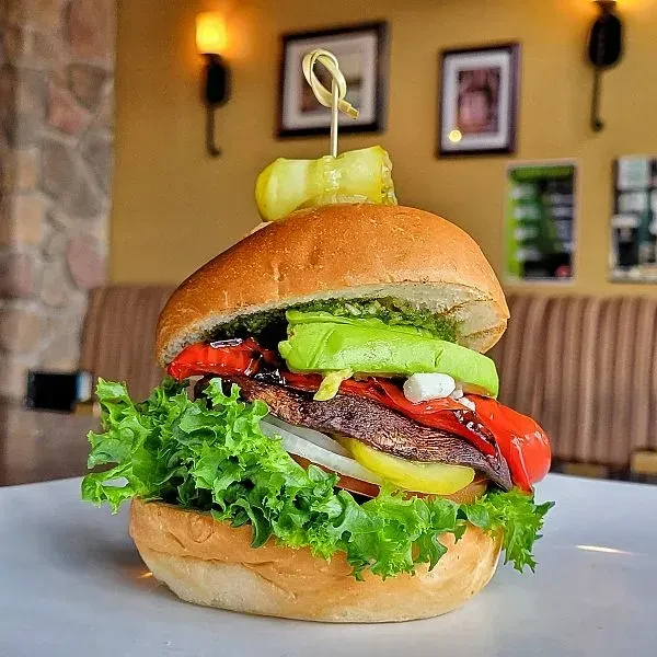 Large burger with pesto, avocado, feta, and pickle spear.