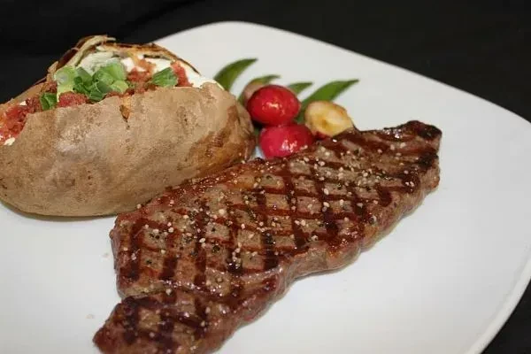 Grilled steak and loaded baked potato with garnishes on a white plate.