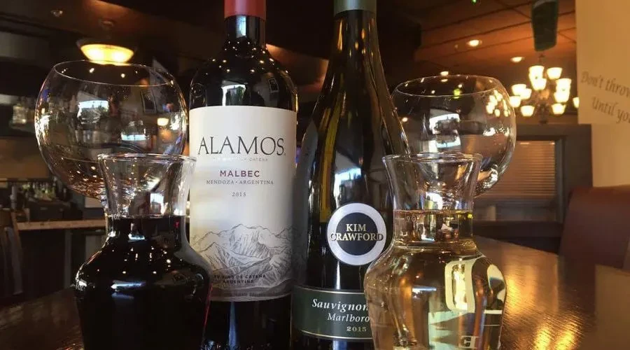 Red and white wine bottles, carafes, glasses on a restaurant table.