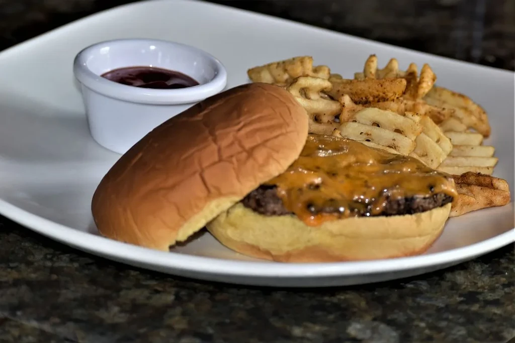 Cheeseburger, waffle fries, and ketchup on a white plate.