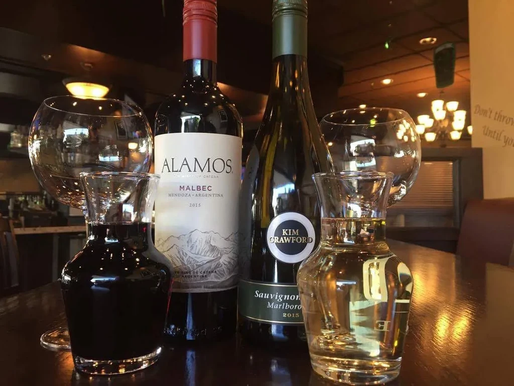 Two wine bottles, carafes, and glasses arranged on a reflective wooden table.