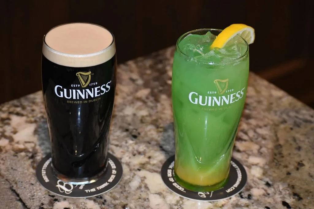 Two Guinness drinks: a stout and a green layered cocktail with lemon.