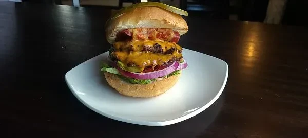 Gourmet double cheeseburger with bacon, cheese, and vegetables on a white plate.