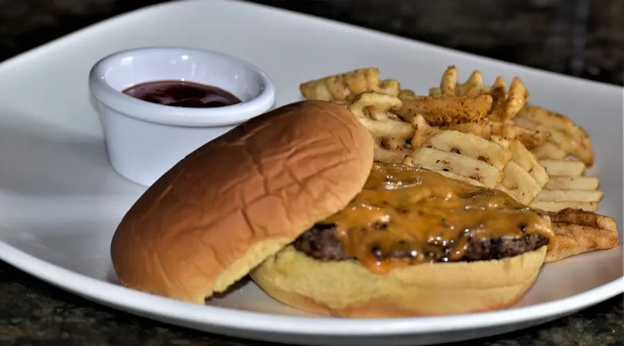 Open-faced cheeseburger, waffle fries, and dipping sauce on a white plate.