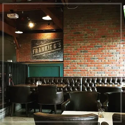 Restaurant interior with exposed brick, "FRANKIE G'S" sign, and leather booths.