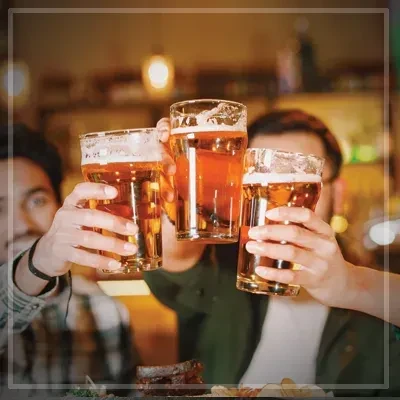 Three hands hold frothy amber beers for a celebratory toast.