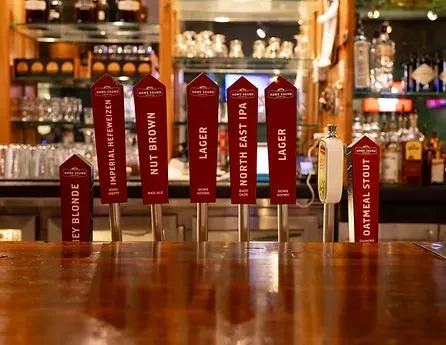 Seven Howe Sound beer tap handles on a polished wood bar.