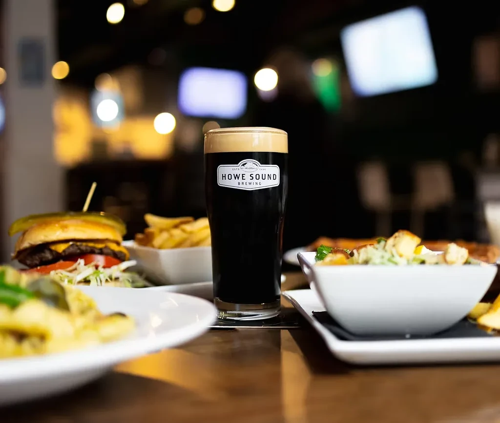 Howe Sound Brewing dark beer, cheeseburger, and fries on a pub table.