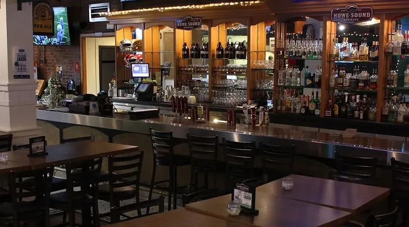 Cozy, dimly lit pub interior with a stocked bar and sports on TV.