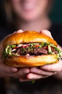 Close-up of a large hamburger with lettuce and tomato, held by hands.