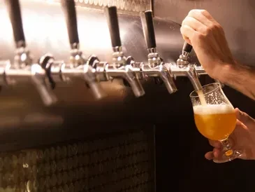 Hands pouring foamy beer from a tap into a glass.