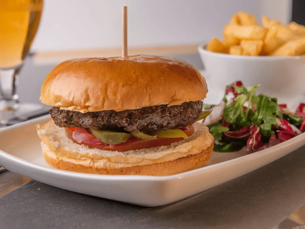 Close-up of hamburger, side salad, crinkle-cut fries, and beer.