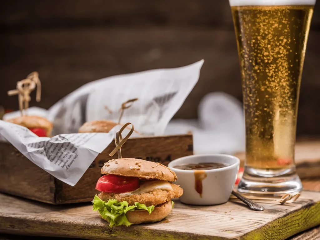 Skewered mini burger, dipping sauce, and frothy beer on wood.