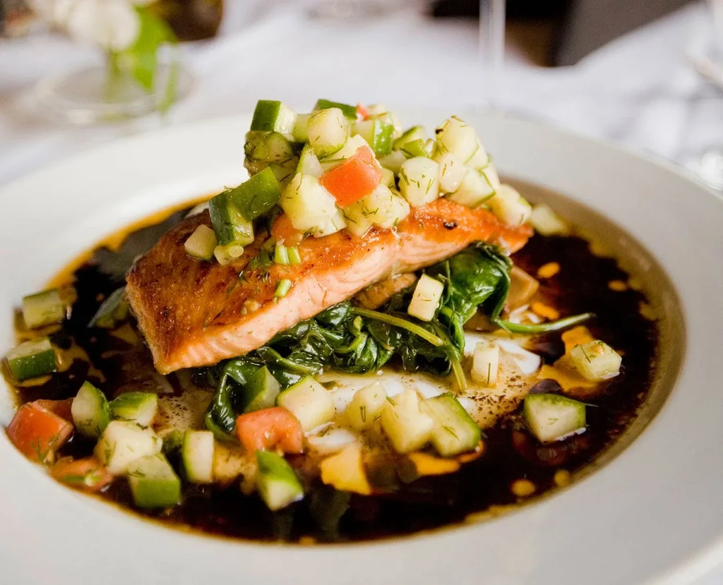 Plated pan-seared salmon, relish, spinach, and mashed potatoes with sauce.