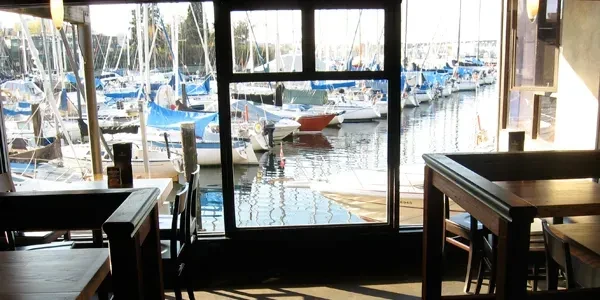 Indoor dining area overlooks a sunlit marina filled with numerous sailboats.