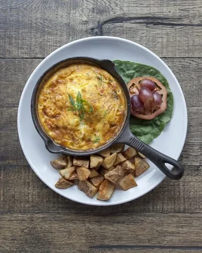 Baked egg skillet, roasted potatoes, and side salad on a wooden table.