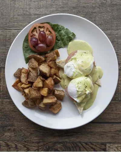 Overhead plate with Eggs Benedict, roasted potatoes, tomato, grapes.