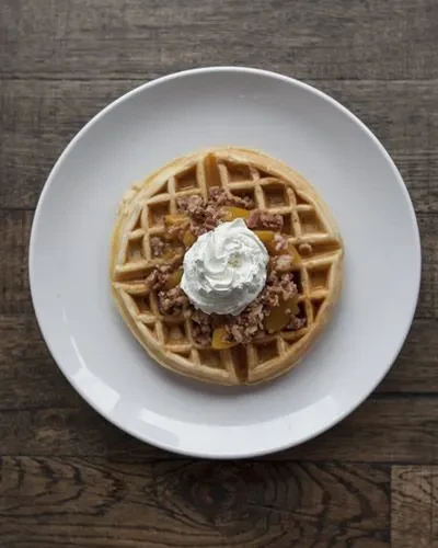 Golden-brown waffle with fruit crumble and whipped cream on wood.