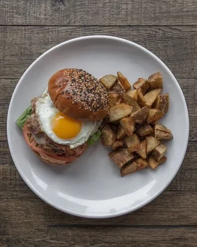 Burger with fried egg, lettuce, and roasted potatoes on a white plate.