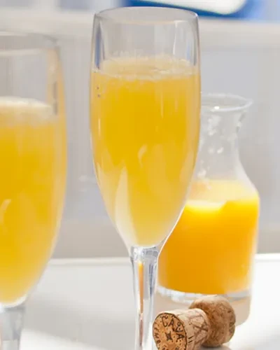 Mimosas in flutes with orange juice carafe and CAVA corks.