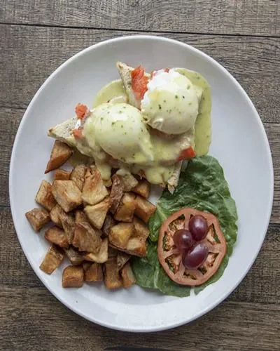 Brunch plate: poached eggs with green hollandaise, potatoes, and fresh salad.