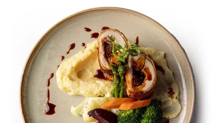 Overhead view: Plated gourmet chicken roulade, mashed potatoes, and colorful vegetables.