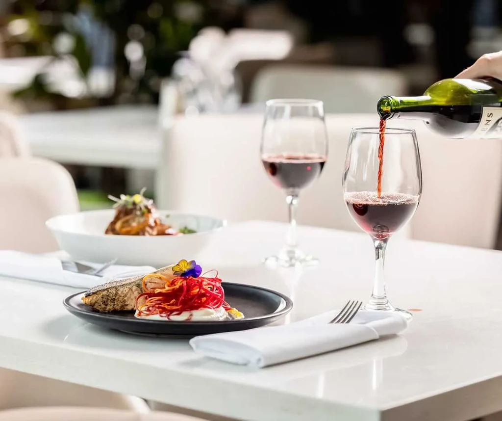 Hand pouring red wine; plated dishes on an elegant restaurant table.