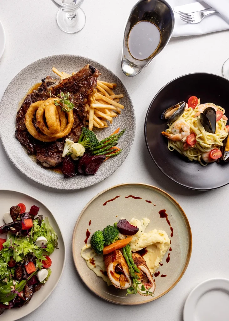 Overhead view of four distinct plated meals on a white table.