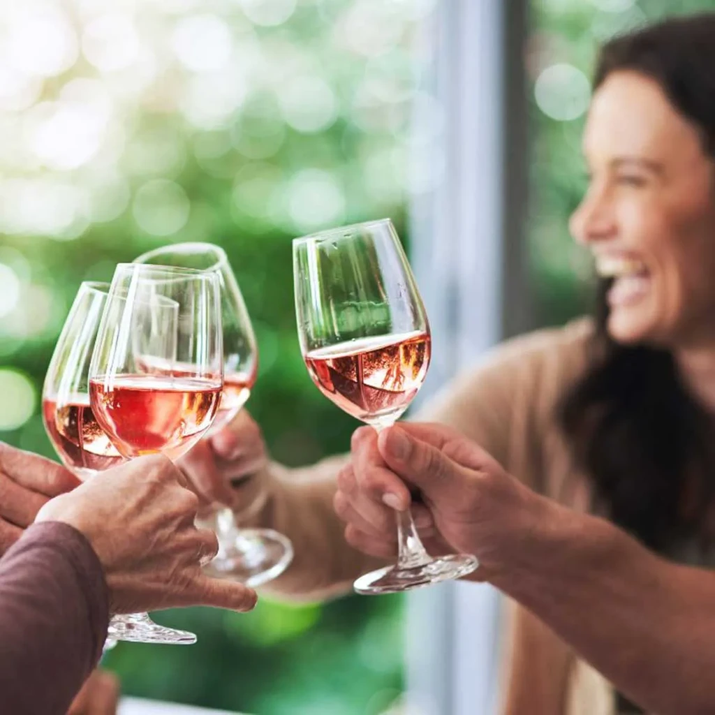 Four hands clinking glasses of rosé wine in a toast.