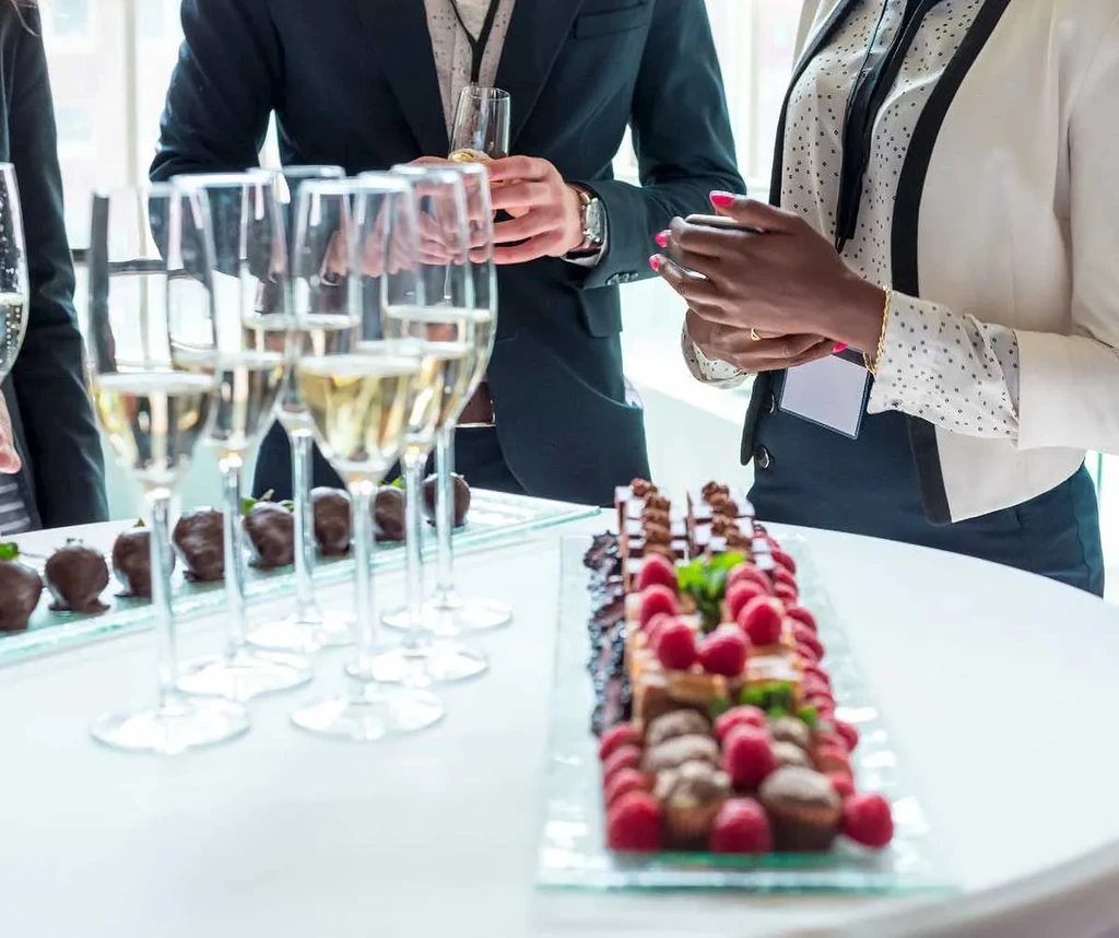 Champagne flutes, chocolate strawberries, and assorted desserts on trays at an event.