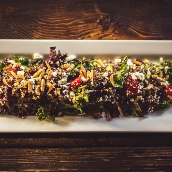 Colorful grain bowl with kale, quinoa, feta, almonds on wood.