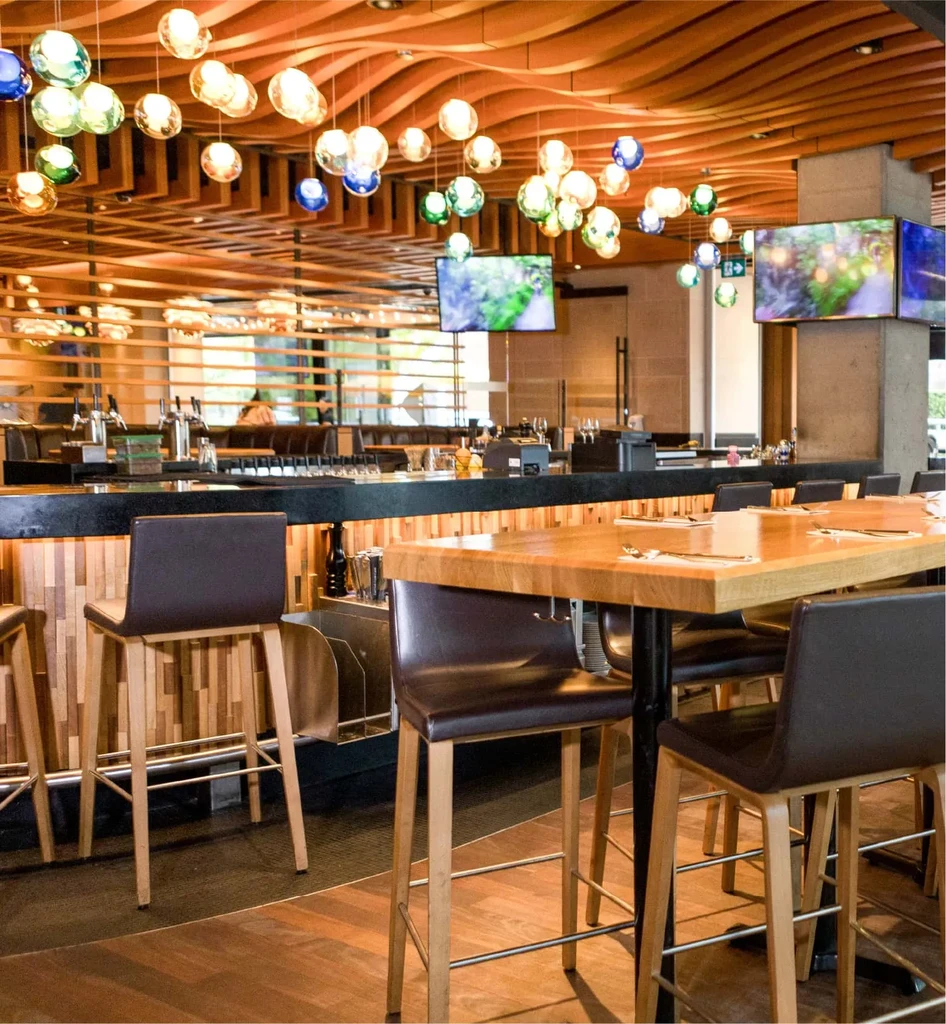 Modern bar and restaurant with wavy wooden ceiling and colorful spherical lights.