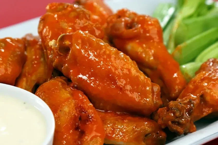 Vibrant orange-red buffalo wings, dipping sauce, and celery.