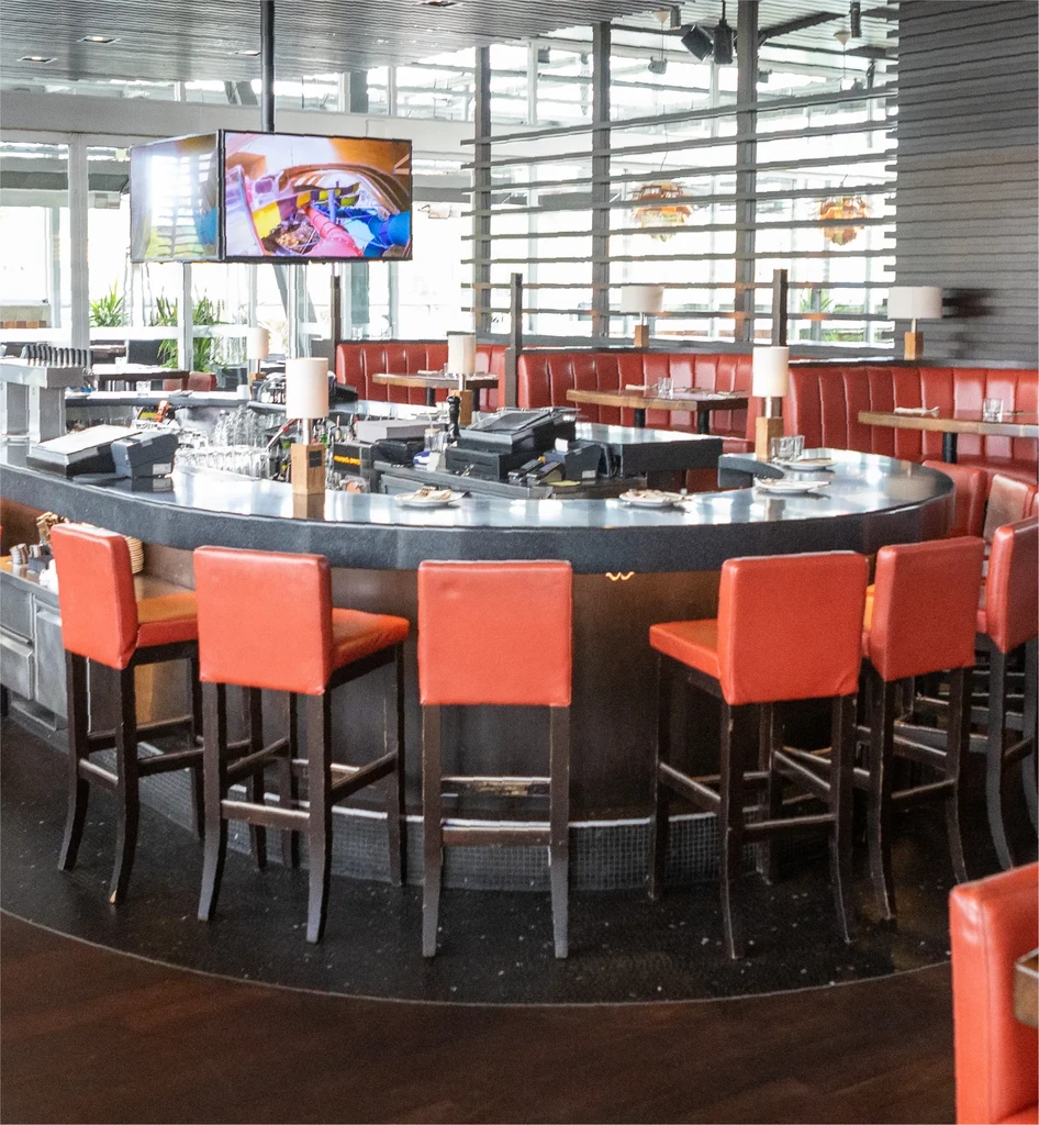 Modern restaurant bar with oval counter, red-orange stools, and booths.