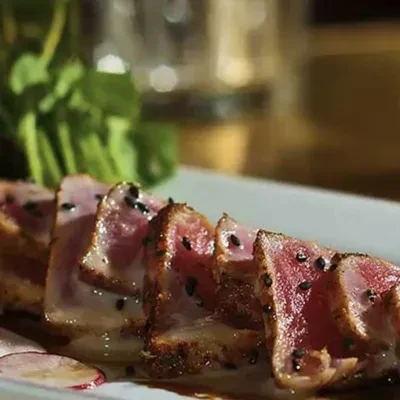 Seared rare tuna slices, garnished with sesame seeds and dark sauce.