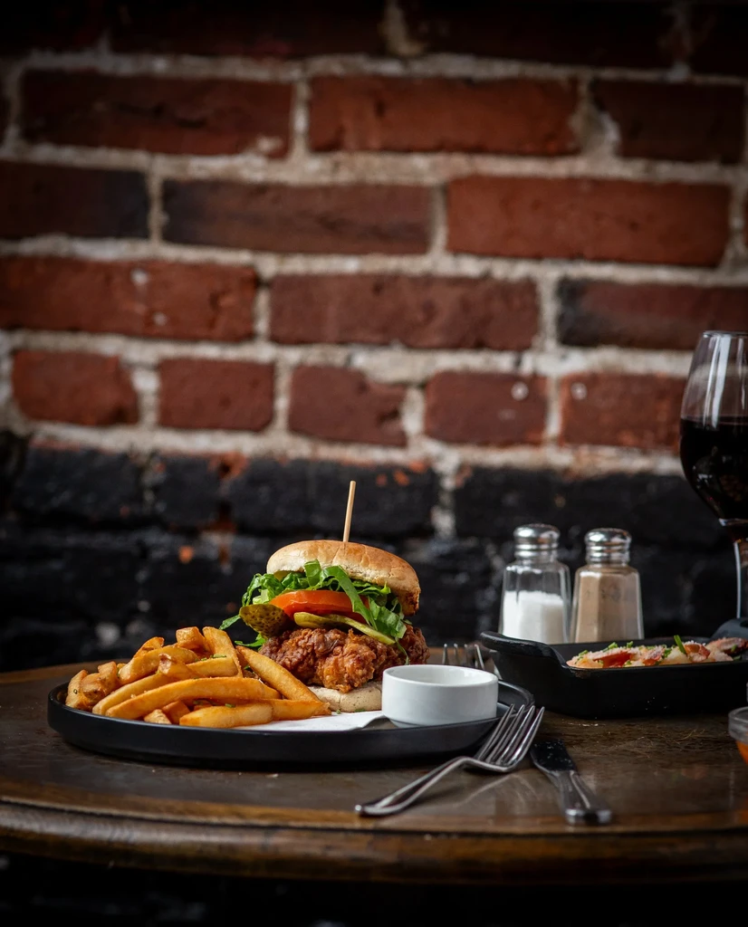 Fried chicken sandwich with golden french fries and red wine.