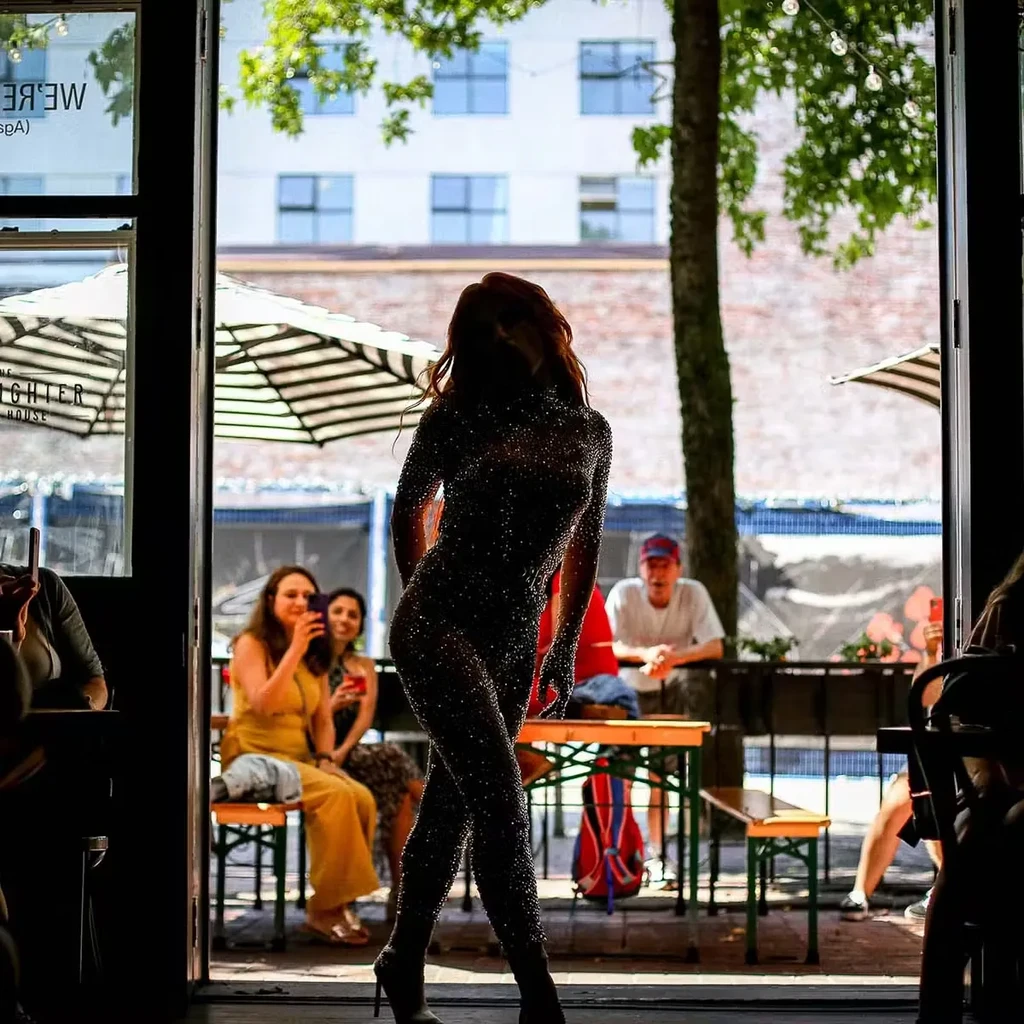Silhouetted performer in sparkling bodysuit striking a pose on an outdoor patio.