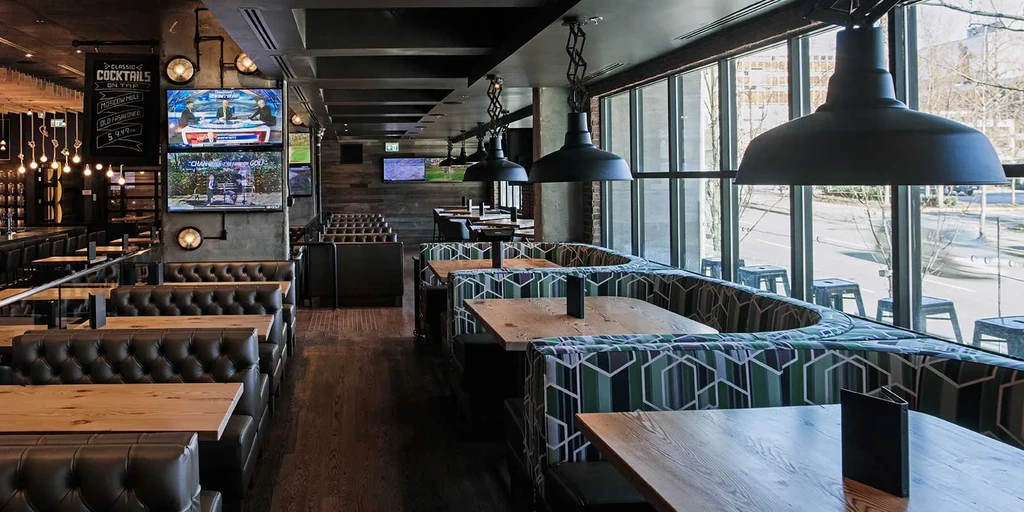 Modern restaurant interior: booths, bar, cocktail chalkboard, and TVs.