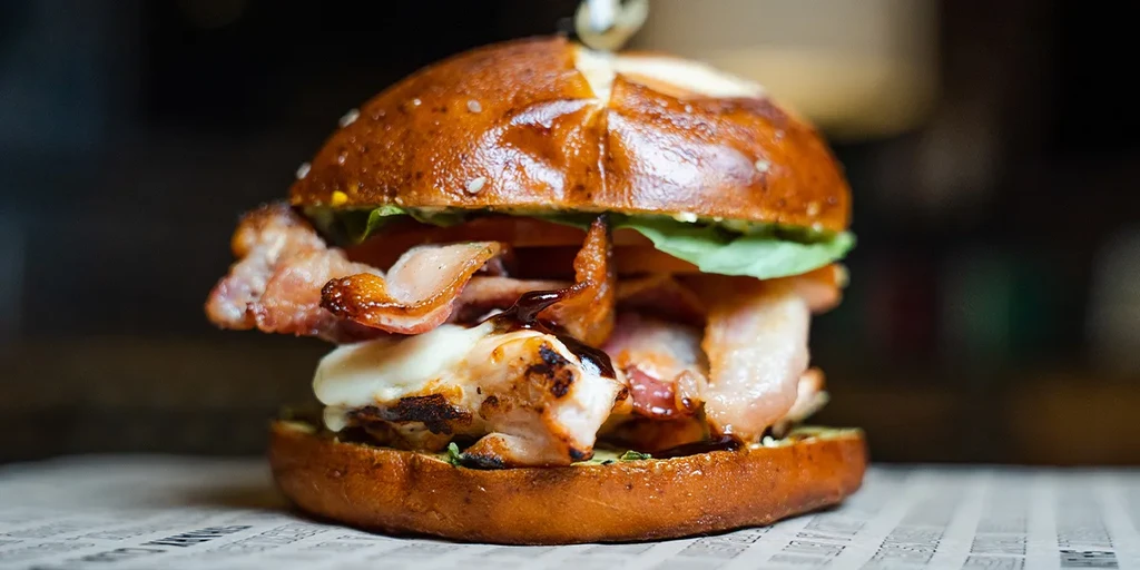 Gourmet burger with pretzel bun, chicken, bacon, cheese, and sauce.