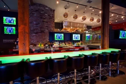 Modern bar with neon green counter, soccer on TVs, and open kitchen.
