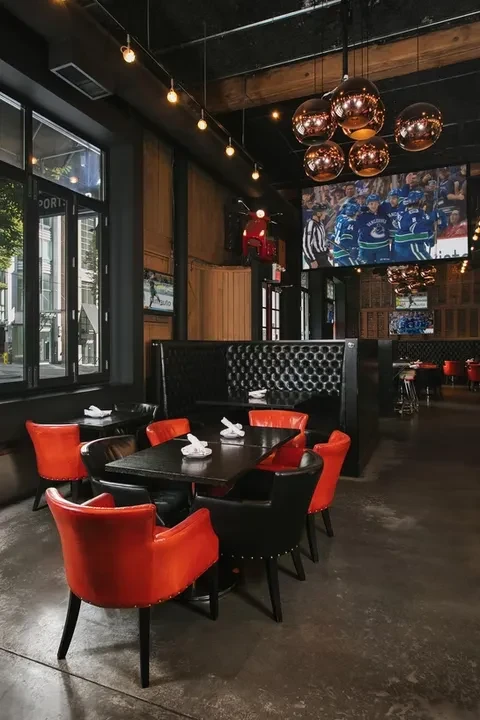 Modern restaurant interior with orange-red seating, hockey game, and scooter.
