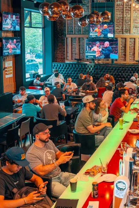 Lively modern sports bar with brick walls, green booths, and TVs.