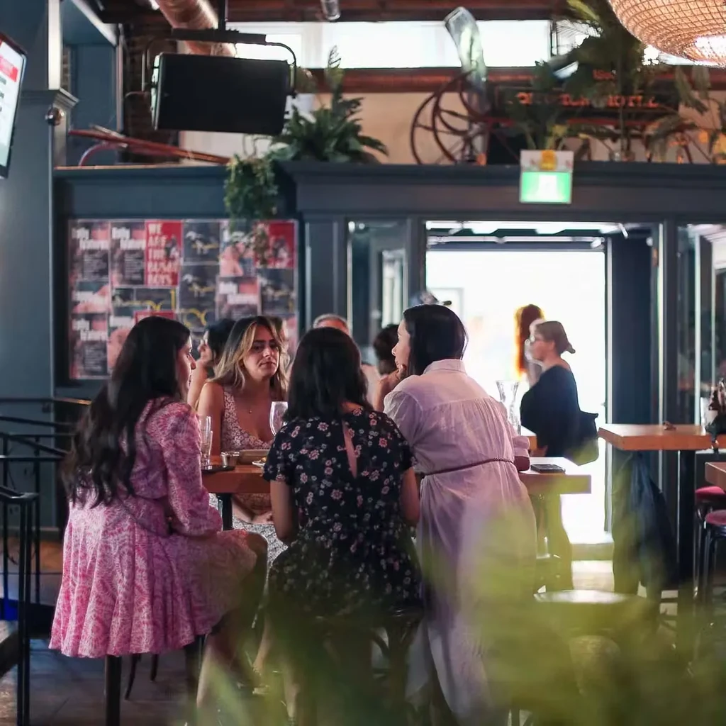 Four women converse at a wooden table in a modern restaurant.