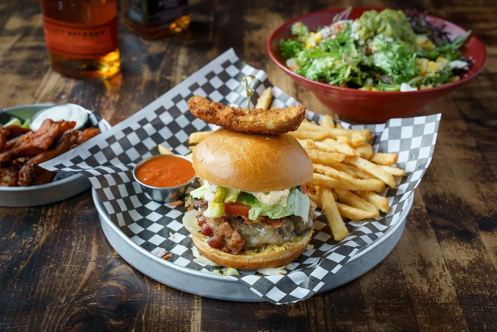 A gourmet burger, fries, wings, and salad on a rustic table.