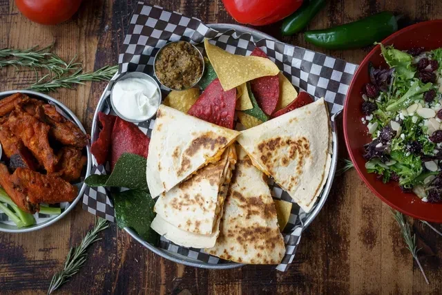 Rustic table spread: Quesadilla, chips, wings, salad, and colorful dips.