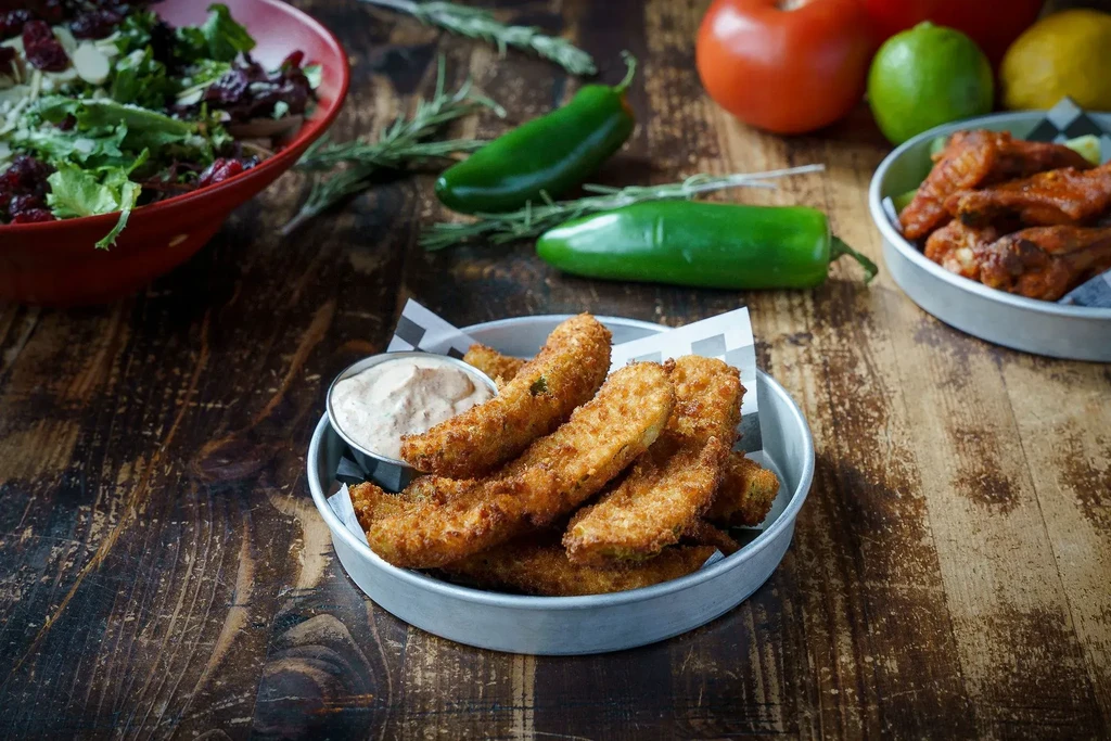 Golden fried items, salad, chicken wings, fresh produce on wooden table.