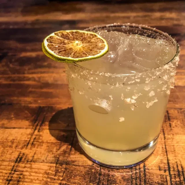 Margarita-like cocktail with salted rim, ice, and dried lime garnish.