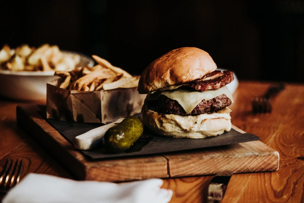 Gourmet hamburger, melted cheese, pickle, and fries on a wooden board.