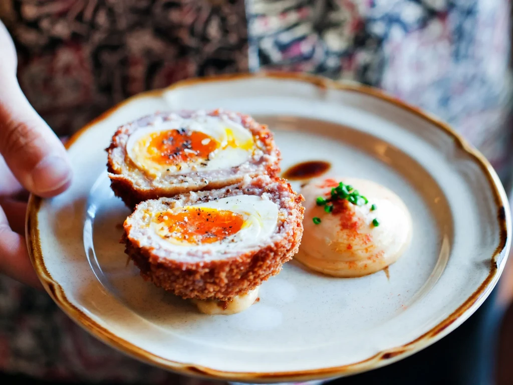 Halved Scotch egg with a runny yolk, crispy coating, sauce, and chives.